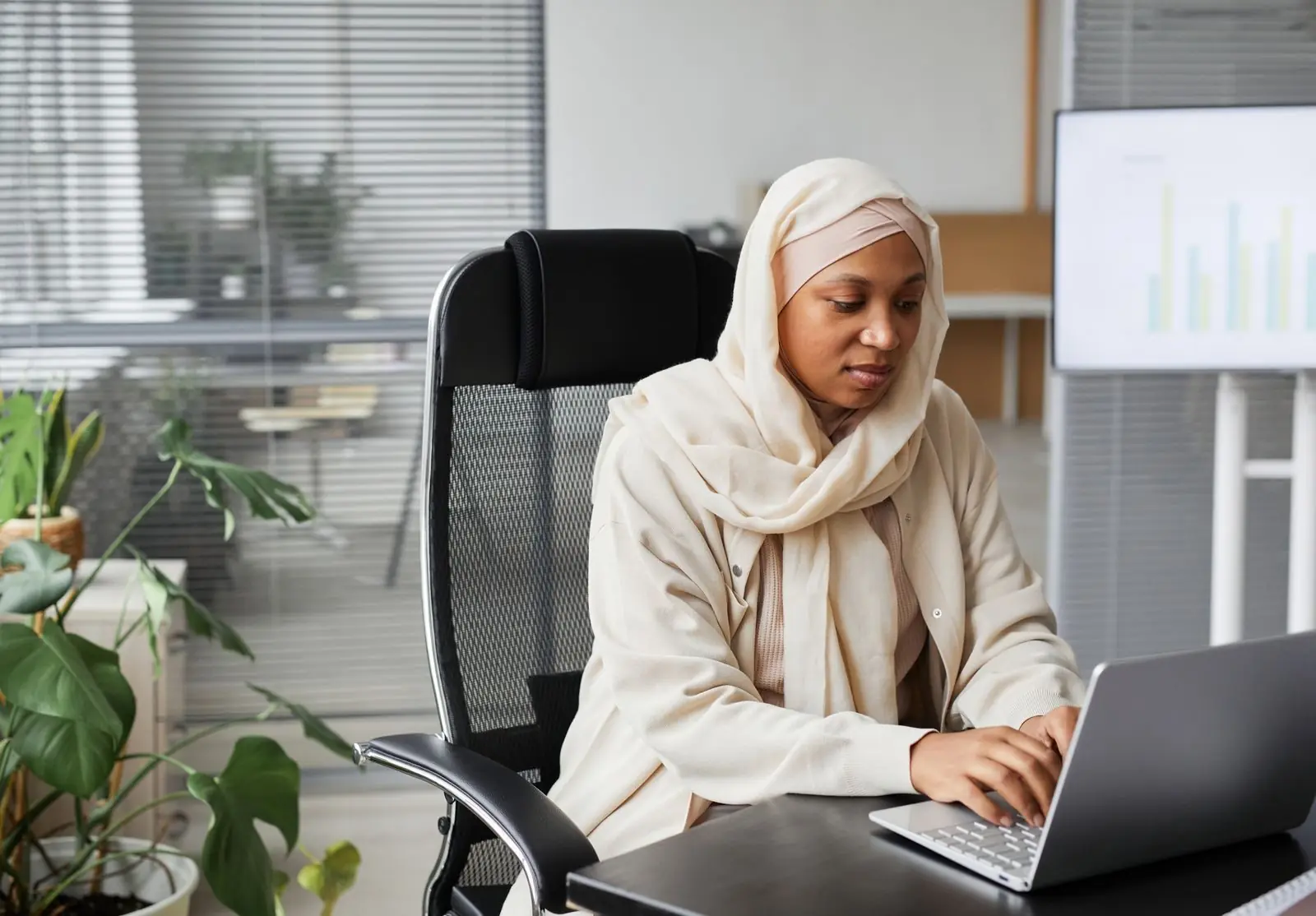 Wanita bertudung bekerja menggunakan komputer riba di pejabat